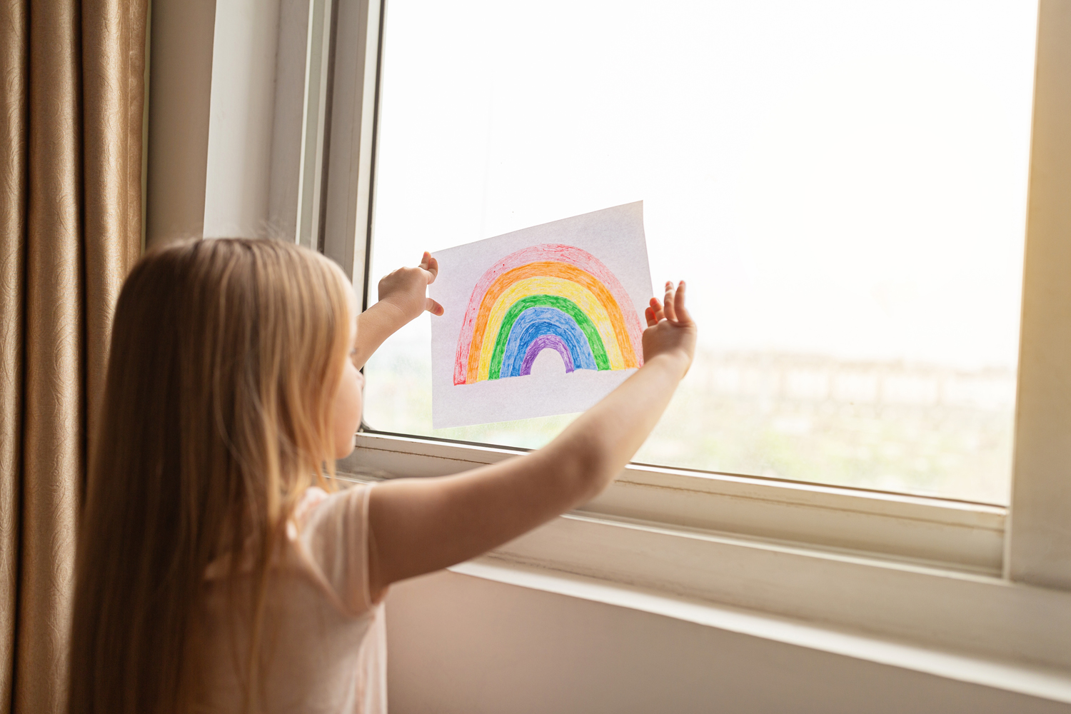 Child with drawing of rainbow at window
